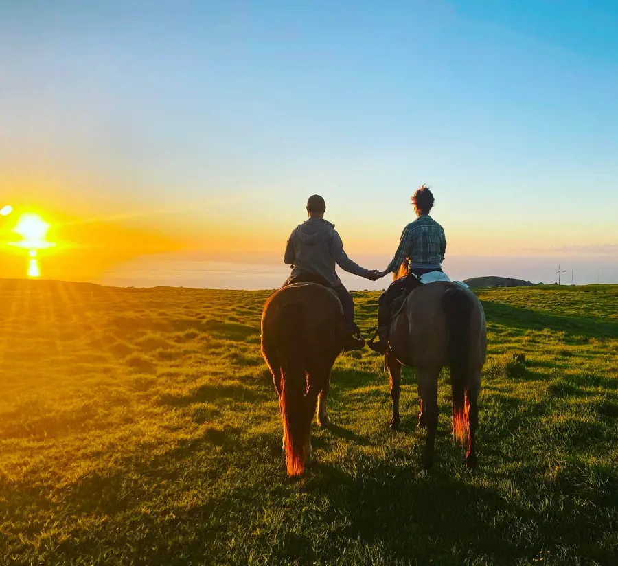 A couple enjoying horseback riding at Na'alapa Stables with a beautiful sunset view