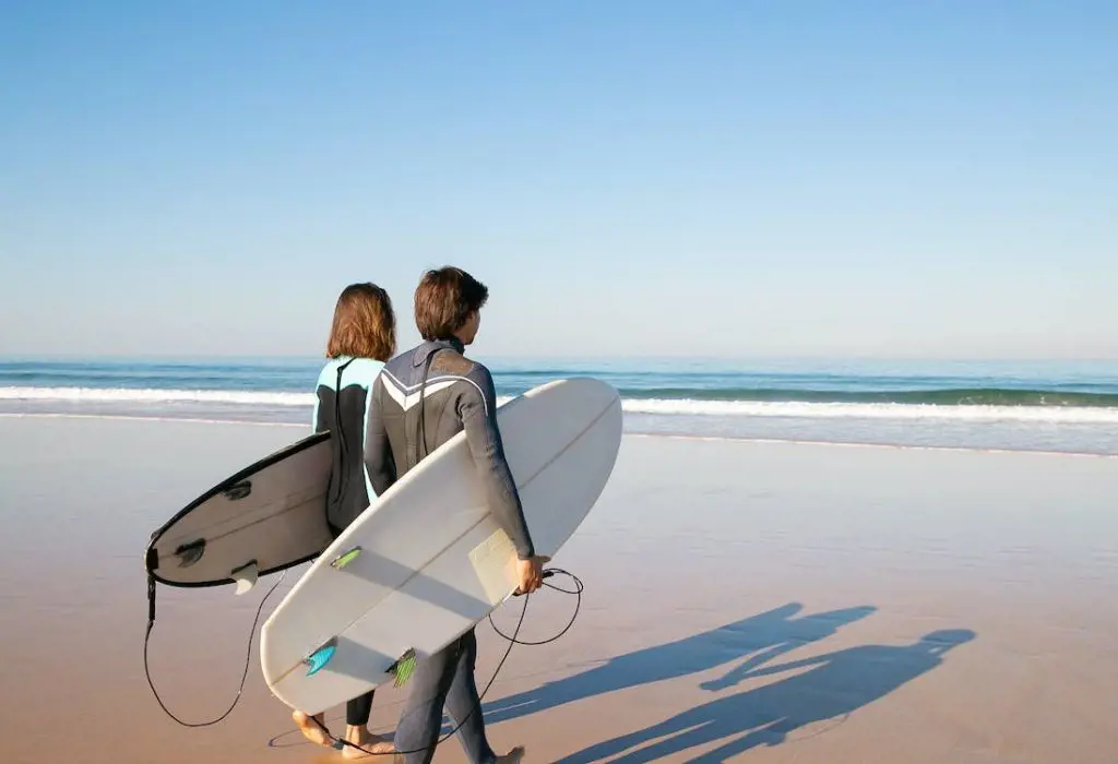 An excited couple carrying surfboards heading towards the ocean for surfing