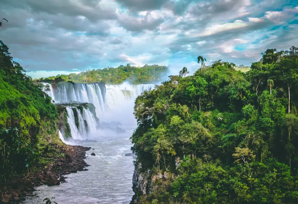 A picturesque view of waterfalls between the tress and under the dreamy cloudy sky