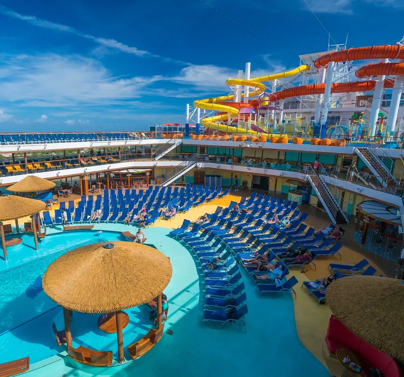 A beautiful view of the waterslide, pool, and sun loungers on the deck of a Carnival Cruise vessel