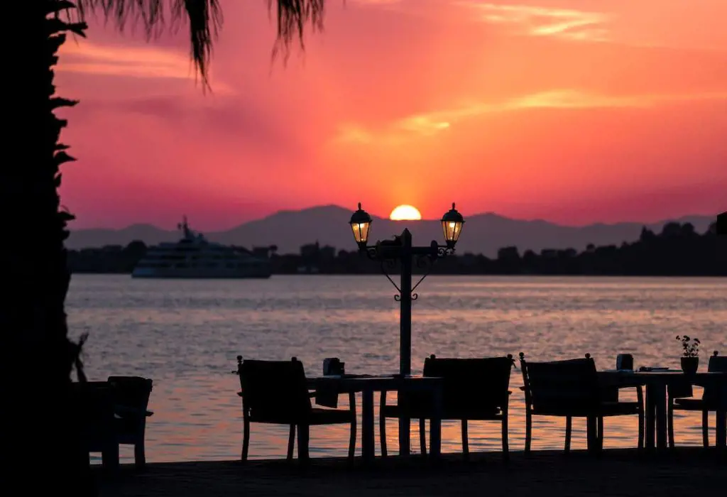 A beautiful arrangement of charis and tables near body of water overlooking the sunset